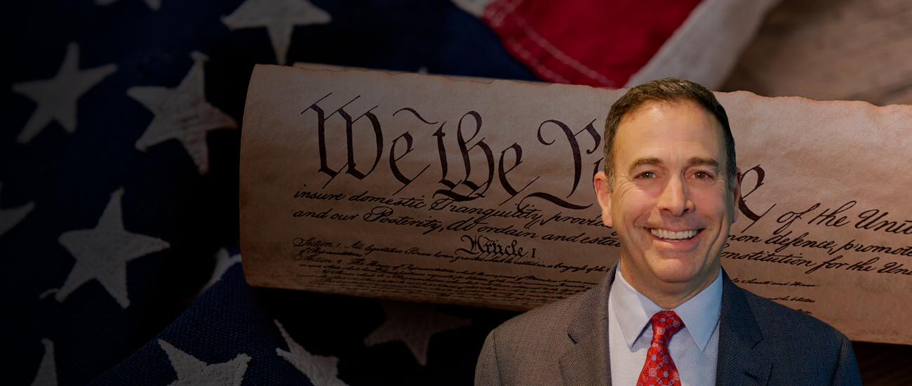 Attorney William Weinberg stands with an illustration of the Constitution in the background