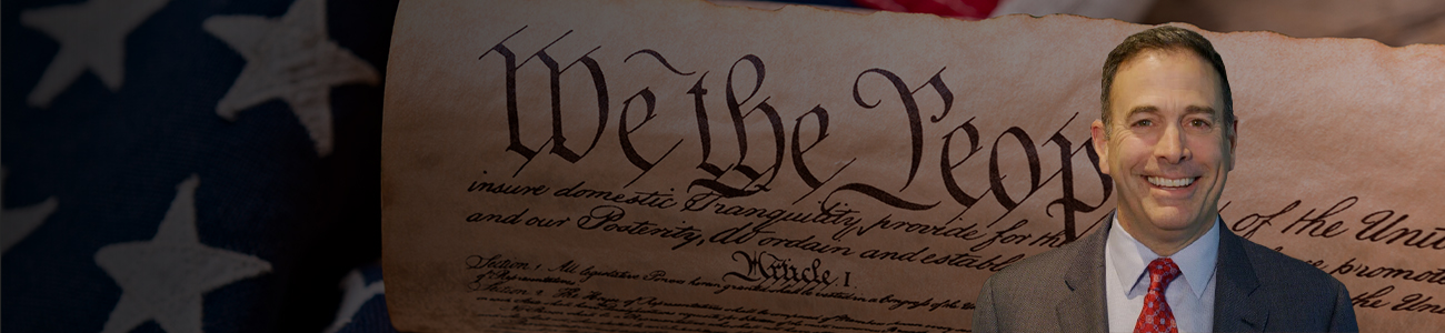 Attorney William Weinberg stands with an illustration of the Constitution in the background