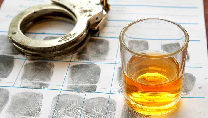 A glass of alcohol beside a pair of handcuffs on a table